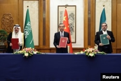 Wang Yi holds up a March 2023 deal in Beijing with Iranian Supreme National Security Council Secretary Ali Shamkhani (right) and Saudi State Minister Musaad bin Muhammad al-Aiban (left).