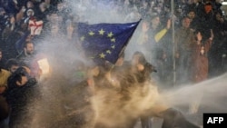 Protesters brandishing a European Union flag are sprayed by a water cannon during clashes with riot police near the Georgian parliament in Tbilisi on March 7, 2023.