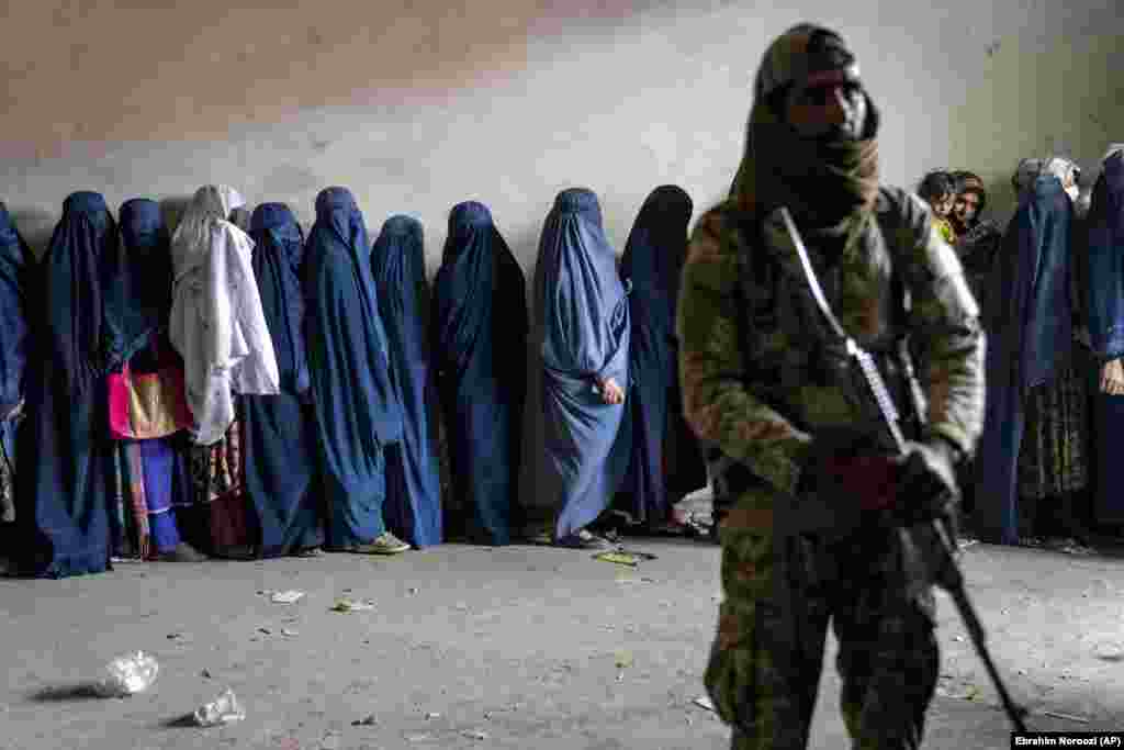 A Taliban fighter stands guard as women wait to receive food rations distributed by a humanitarian aid group in Kabul in May. Aid groups estimate that some 30 million Afghans are in need of assistance.