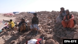 People affected by the recent earthquakes sit on the debris of demolished houses in the Zendajan district of Afghanistan's western Herat Province on October 16.