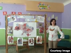 Olesya Dorofyeyeva, a teacher of foreign literature and events coordinator at Harant, stands by a project showing traditional dress at the now-ruined school building in Lysychansk.