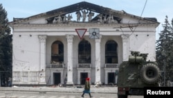 A woman walks next to an armored vehicle manned by pro-Russian troops outside the desroyed Donetsk Academic Regional Drama Theater in Mariupol on April 10. 