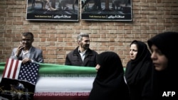 Iranians stand under anti-American posters as they attend a demonstration outside former U.S. Embassy in Tehran on November 4 depicting an American and Iranian negotiator sitting together.