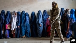 A Taliban fighter stands guard as women wait to receive food rations distributed by a humanitarian aid group in Kabul in May 2023. (file photo)