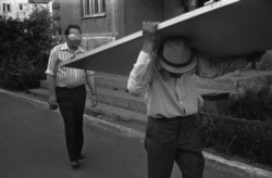 A man in a mask and a man carrying a door in July 1988.