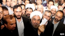 Presidential candidate Hassan Rohani (center) shows his ballot to the media as he casts his vote at the Imam-Reza mosque in southern Tehran.