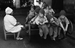 Staff watch over children in a rocker at an orphanage in May 1981. The children are dressed the same because their clothes would have been acquired in bulk at the same time.