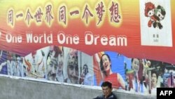 A man sits under a poster for the 2008 Beijing Olympic Games on a street in Xinjiang in August 2008.