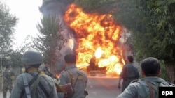 Afghan police stand by as flames rise from an oil tanker in Kunduz hit by Taliban rockets