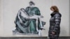 A woman walks past a mural depicting a medical worker in a pose like that of Michelangelo's famous Pieta sculpture, on a wall near a vaccination center in the Bulgarian capital, Sofia.