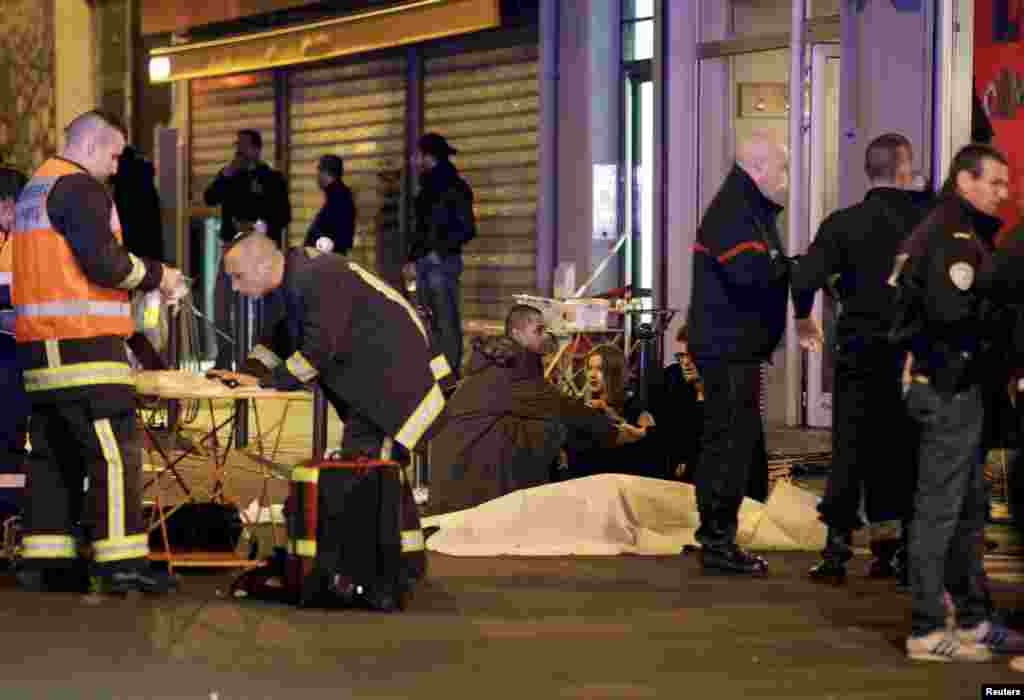 A French rescue worker checks his laptop computer as three people consol each other over the body of a shooting victim.&nbsp;