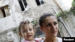 A woman carrying her child stands in front of a state-owned house given to refugees in Tbilisi. (file photo)