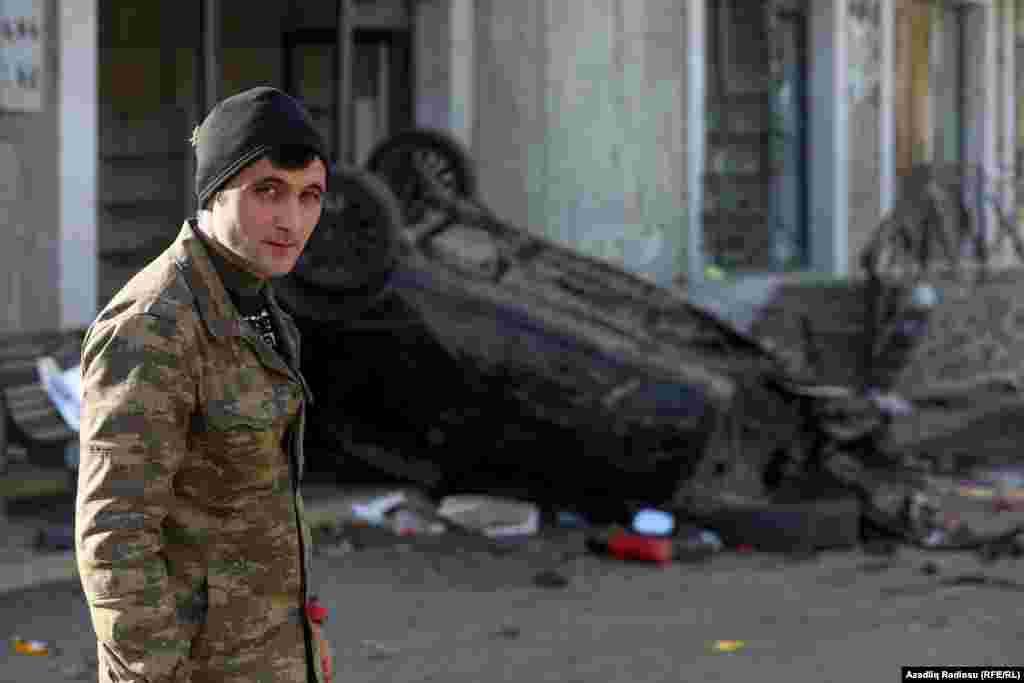 An Azerbaijani soldier poses in front of a damaged car in Hadrut.