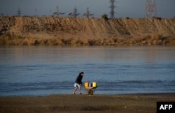 An Afghan moves water containers in a wheelbarrow alongside the Amu River, which forms the border between Afghanistan and Uzbekistan in Afghanistan's northern Balkh Province.