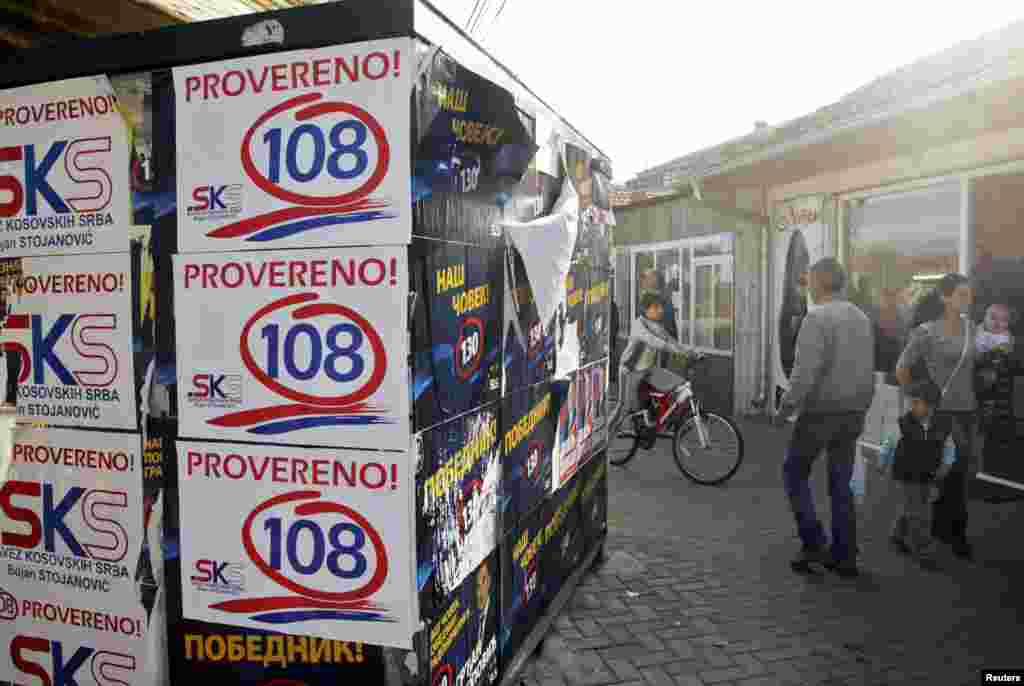 Kosovar Serbs walk past campaign posters for the Alliance of Kosovo Serbs and the Independent Liberal Party in Gracanica.