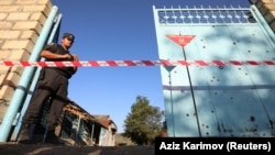 An Azerbaijani law enforcement officer guards a yard with an unexploded shell next to a house that locals said was damaged during recent shelling by Armenian forces.