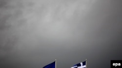 The EU and Greek flags fly in front of dark rain and thunderstorm clouds in Athens in early October.