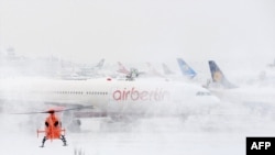 A helicopter lands next to an Air Berlin plane at the airport of Duesseldorf, Germany, one of many airports struggling to cope with the weather.