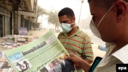 Iraqi men wearing surgical masks against a vicious sandstorm read an Iraqi paper with news of U.S. Vice President Joe Biden's visit on July 5.