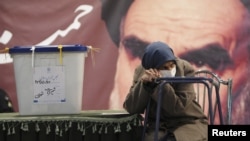 A sick woman waits beside the ballot box as election officials register her so she can cast her ballot in Tehran on March 2.