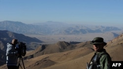 A security guard (right) keeps watch as a foreign journalist films at Kotal-e Kherskhan in Wardak Province. Aid agencies have threatened to pull out of Afghanistan over the ban.