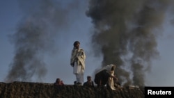 Smoke rises past residents standing on the wall of a truck terminal where NATO fuel tankers were set ablaze in Quetta on December 9.