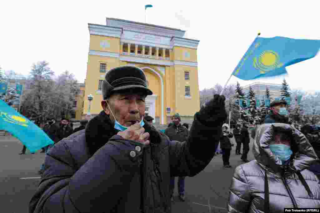 Қазақстанның жалаушасын ұстаған ер кісі сөйлеушілерге қолдау ретінде ысқырып тұр.