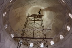 A worker clings to a safety rope as he plasters the roof of a mosque.