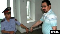 A police officer leads opposition activist Yermek Narymbaev to court in handcuffs.