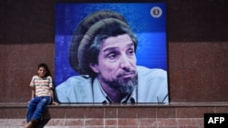 An Afghan boy in Kabul sits next to a poster bearing the image of the late resistance leader Ahmad Shah Masud, who fought for a decade against Soviet invaders.