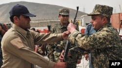 A Blue Hackle officer (left) hands over a gun to a soldier from the Afghan Public Protection Forces during a ceremony on the outskirts of Kabul in March.