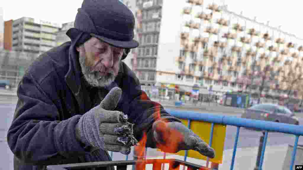 A homeless man warms up near an outside coal fire on a street in Warsaw.