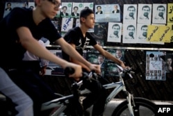 Iranian youth ride their bicycles past campaign posters in Tehran.