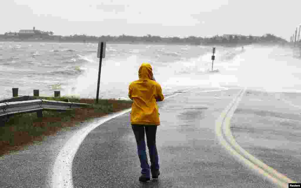 A woman takes photographs of waves pushed onto a road by Hurricane Sandy in Southampton, New York.