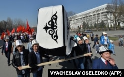 People wear kalpaks and carry a giant one and national flags during a rally on Flag/Kalpak Day in Bishkek on March 5, 2016.