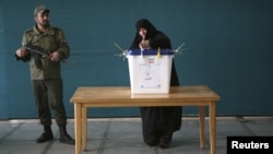 A woman from the Iranian city of Qom casts her vote in parliamentary elections on March 2 as a policeman stands guard. 