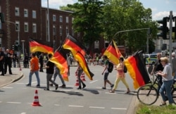 A group of demonstrators opposed to the unveiling carrying German flags. The Lenin monument is visible, covered in a red sheet, in the background.