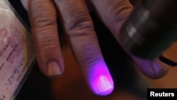 An election official checks a voter's fingers for invisible ink at a polling station during the parliamentary election in the village of Sartichala, Georgia on October 1, 2012.