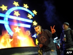 Masked protesters warm themselves at a fire after setting up camp in front of the European Central Bank in Frankfurt.