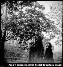 A child appears to notice an agent secretly photographing her mother.