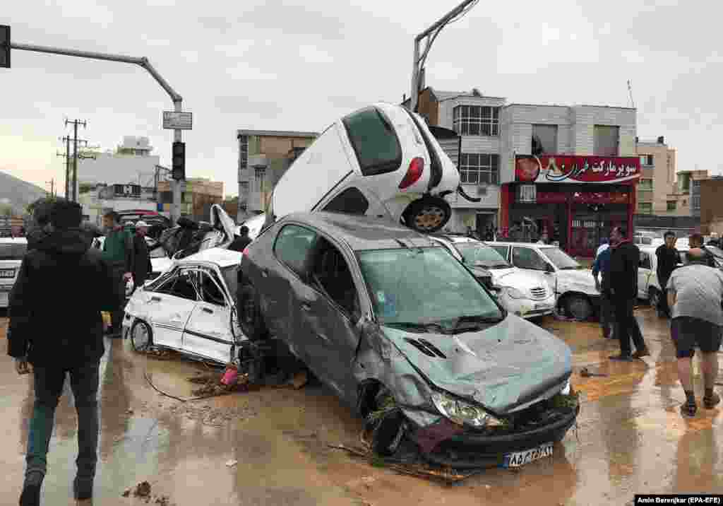 People stand near destroyed cars in the city of Shiraz on March 25.