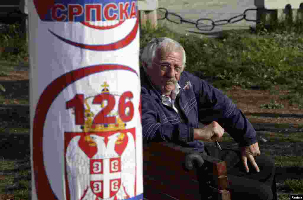 A Kosovar Serb sits near a poster for the Serbian Citizens' Initiative political party in the town of Gracanica, which is inhabited by a Serbian minority.