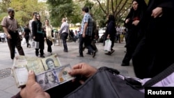 A money changer displaying U.S. and Iranian banknotes on the streets of Tehran