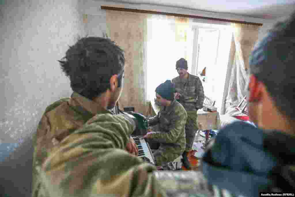 An Azerbaijani soldier plays the piano, watched by his comrades, in an abandoned house in Hadrut.