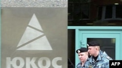 Two Russian antiriot policemen pass by the Yukos oil giant's logo during an auction for the sale of the company's key assets at Yukos's Moscow headquarters.