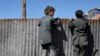 Afghan boys look over a metal barrier at people receiving food supplies during a distribution of humanitarian aid for families in need in Kabul on February 16.