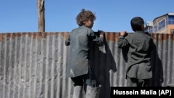 Afghan boys look over a metal barrier at people receiving food supplies during a distribution of humanitarian aid for families in need in Kabul on February 16.