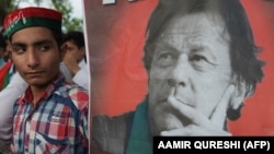 A supporter of Pakistan's cricketer-turned politician and head of the Pakistan Tehrik-e Insaf (Movement for Justice) party Imran Khan stands next to poster with a picture of Khan as they gather near his residence in Islamabad on July 26.