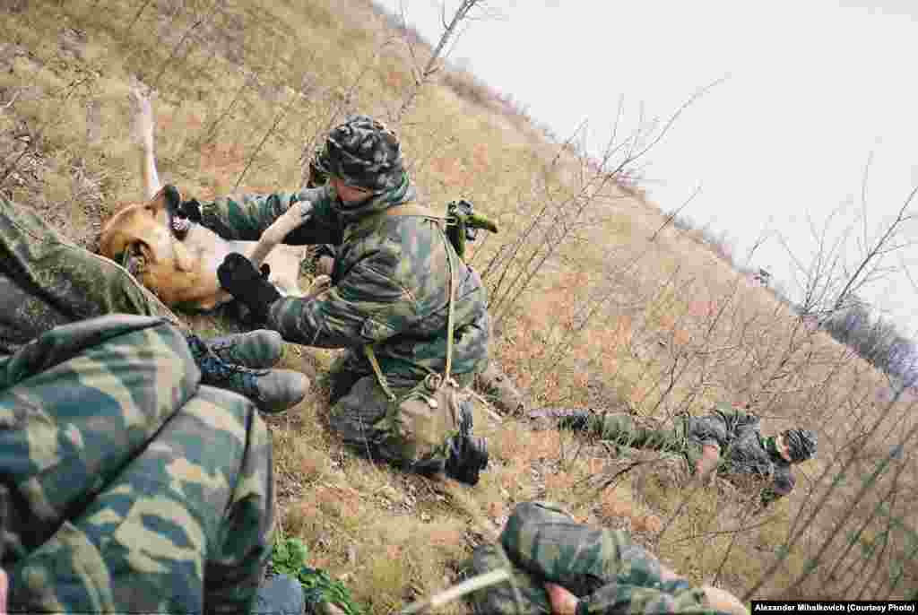 One soldier plays with a dog named Kalashnikov while others fall asleep on the grass during a short break. 