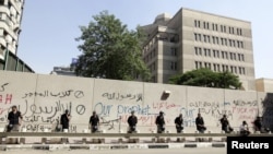 Egyptian security personnel stand guard near a wall with graffiti at the U.S. Embassy in Cairo, where protesters gathered to condemn a film being produced in the United States that insulted the Prophet Mohammad.